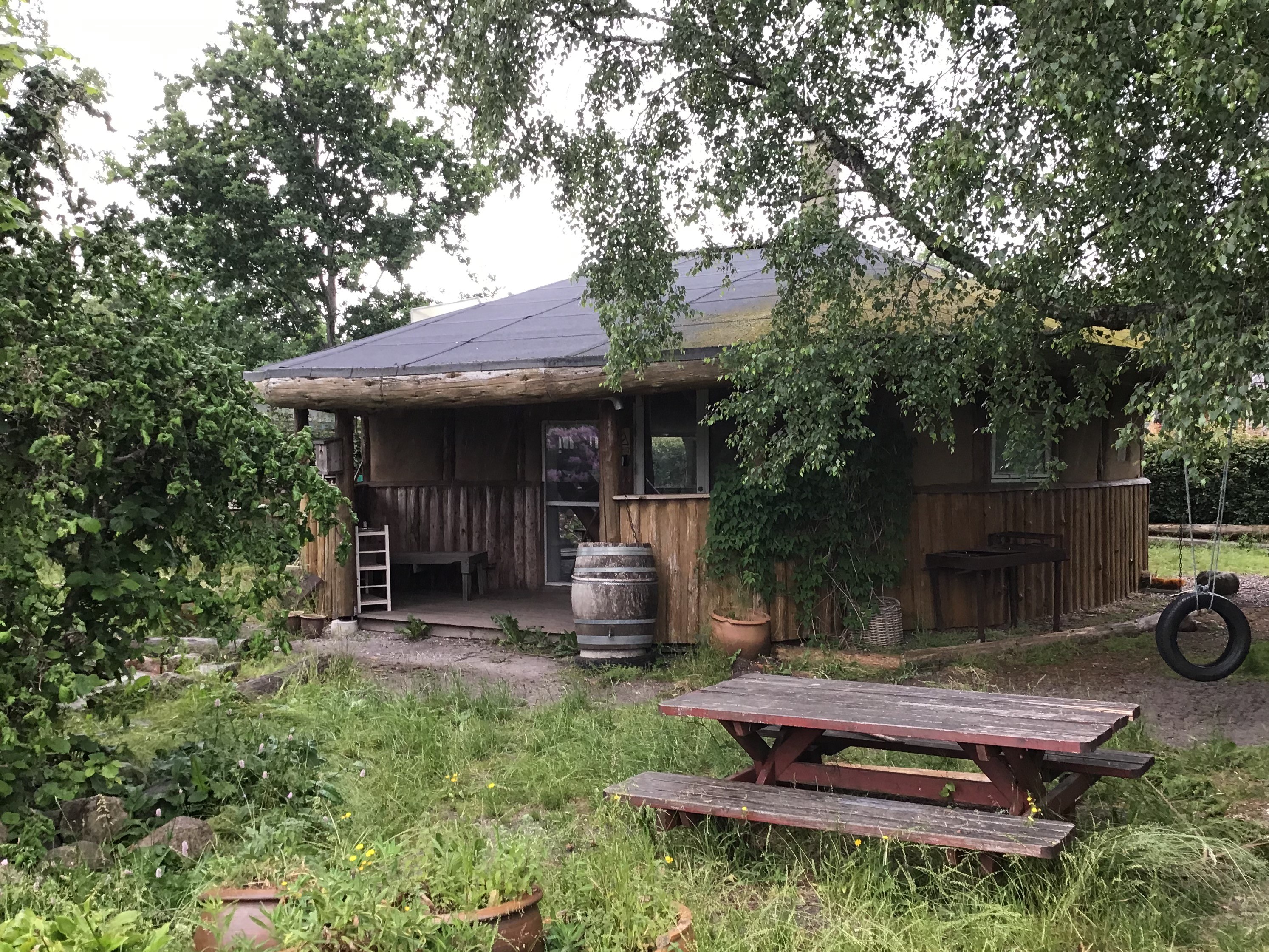 Kolonihaven og huset. Der er legeredskaber i haven og et bord og bænke sæt.